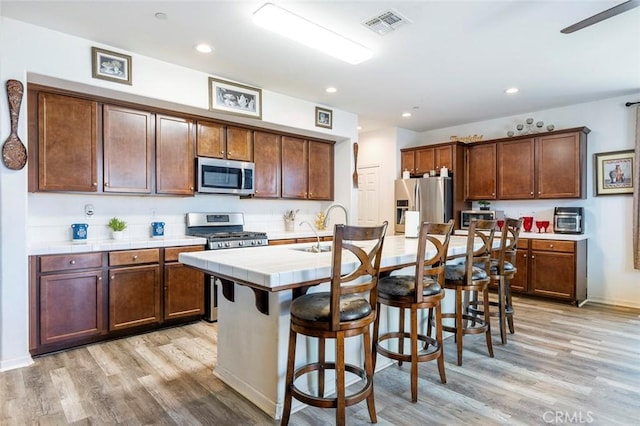 1413 La Quinta Way, Madera, CA 93638 - kitchen featuring stainless steel appliances, tile counters, light wood-style flooring, a breakfast bar area, and recessed lighting