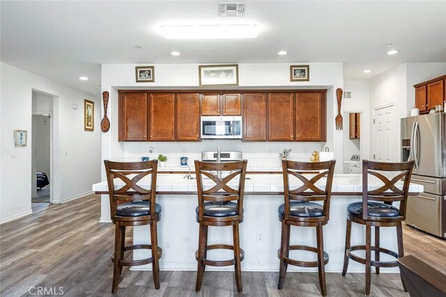 1413 La Quinta Way, Madera, CA 93638 - kitchen featuring stainless steel appliances, a center island with sink, recessed lighting, wood finished floors, and light countertops