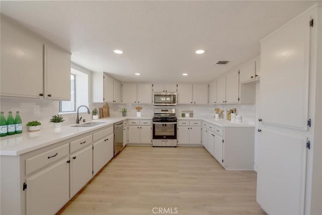 16754 Pauhaska Rd, Apple Valley, CA 92307 - kitchen featuring appliances with stainless steel finishes, a sink, decorative backsplash, light wood-style flooring, and white cabinetry