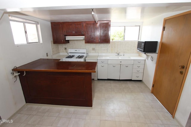 5021 Alvarado St, Carpinteria, CA 93013 - kitchen featuring gas range gas stove, black microwave, under cabinet range hood, a peninsula, and light flooring