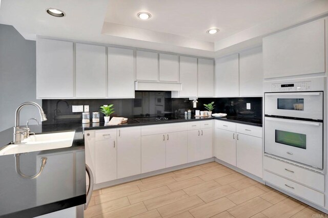 55 Jasmine Creek Dr, Corona Del Mar, CA 92625 - kitchen featuring a raised ceiling, dark countertops, double oven, tasteful backsplash, and white cabinetry