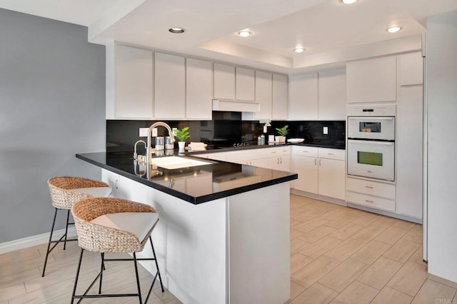 55 Jasmine Creek Dr, Corona Del Mar, CA 92625 - kitchen featuring a peninsula, decorative backsplash, a tray ceiling, dark countertops, and double oven