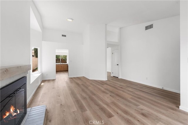 37109 Daisy St, Palmdale, CA 93550 - unfurnished living room featuring a glass covered fireplace, light wood finished floors, baseboards, and a high ceiling