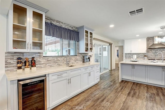 12081 Martha Ann Dr, Los Alamitos, CA 90720 - kitchen featuring wine cooler, wall chimney exhaust hood, tasteful backsplash, light wood finished floors, and light countertops