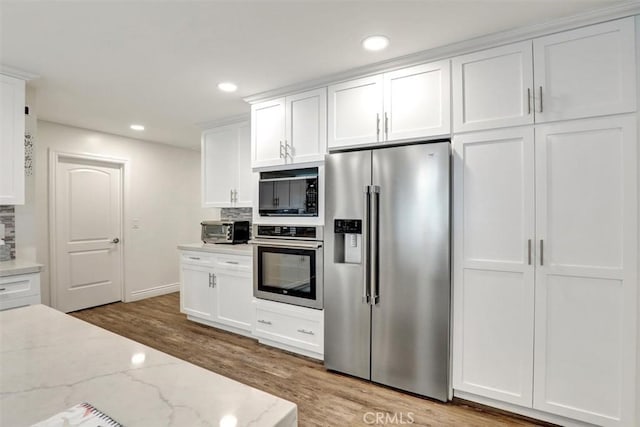 12081 Martha Ann Dr, Los Alamitos, CA 90720 - kitchen with stainless steel appliances, wood finished floors, white cabinetry, recessed lighting, and light stone counters