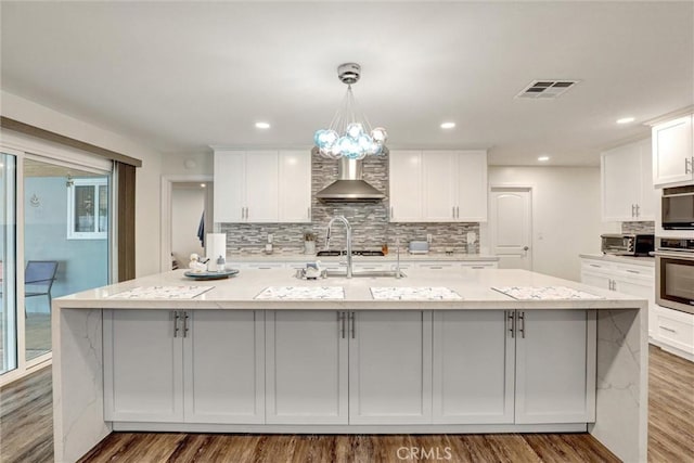 12081 Martha Ann Dr, Los Alamitos, CA 90720 - kitchen with wall chimney exhaust hood, stainless steel oven, a large island with sink, tasteful backsplash, and wood finished floors