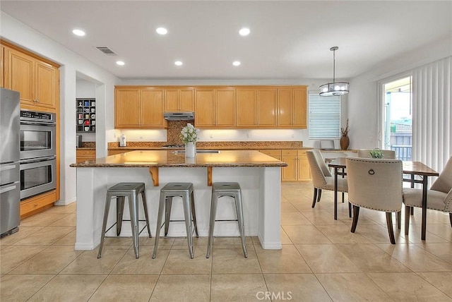 4451 Terry St, Chino, CA 91710 - kitchen featuring stainless steel appliances, a center island, under cabinet range hood, a breakfast bar, and light tile patterned flooring