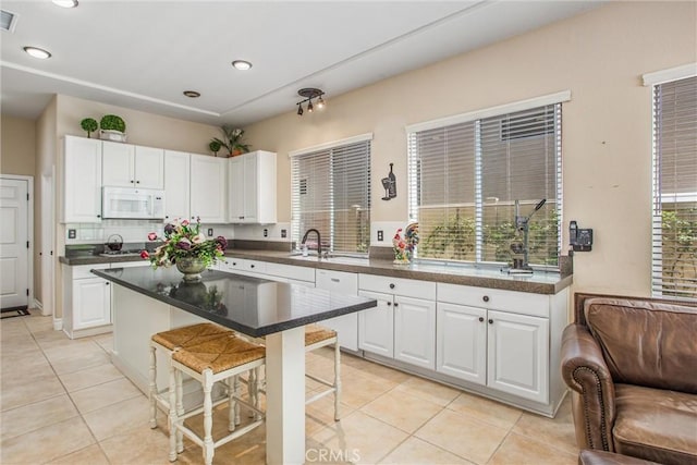 2012 Melbourne Cir, Banning, CA 92220 - kitchen with white microwave, a kitchen breakfast bar, light tile patterned flooring, white cabinets, and recessed lighting