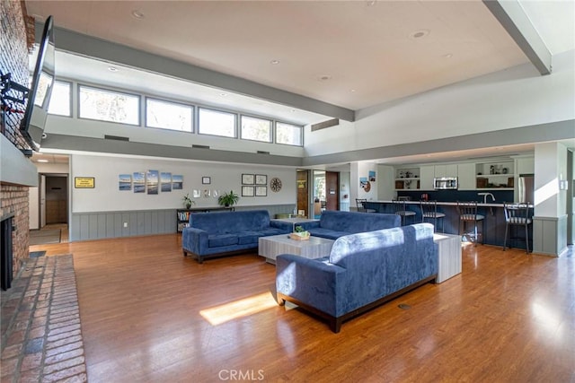3605 W Hidden Ln Unit 112, Rolling Hills Estates, CA 90274 - living room featuring a brick fireplace, a high ceiling, wood finished floors, beam ceiling, and a wainscoted wall