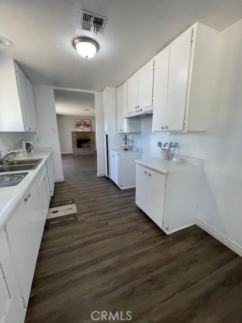 15577 Nisqualli Rd, Victorville, CA 92395 - kitchen featuring under cabinet range hood, light countertops, a fireplace, white cabinets, and dark wood-style floors