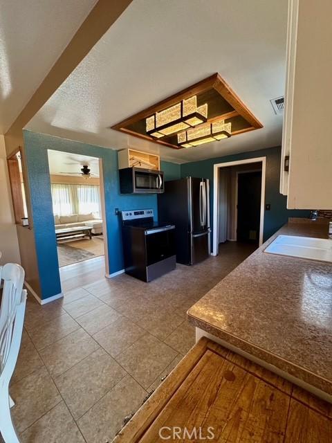 3646 Kirkwood Rd, Corning, CA 96021 - kitchen featuring black electric range, stainless steel microwave, freestanding refrigerator, tile patterned floors, and a ceiling fan