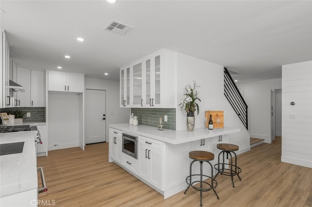 16791 Glenhaven Ln, Huntington Beach, CA 92647 - kitchen with tasteful backsplash, a kitchen breakfast bar, glass insert cabinets, light wood finished floors, and white cabinets