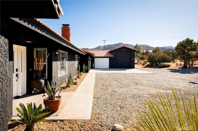 58916 Carmelita Cir, Yucca Valley, CA 92284 - view of side of property with a chimney, a mountain view, stucco siding, gravel driveway, and a tile roof