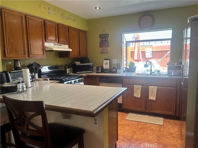 116 Evergreen Pl, Perris, CA 92571 - kitchen featuring stainless steel appliances, tile counters, under cabinet range hood, a peninsula, and brown cabinets