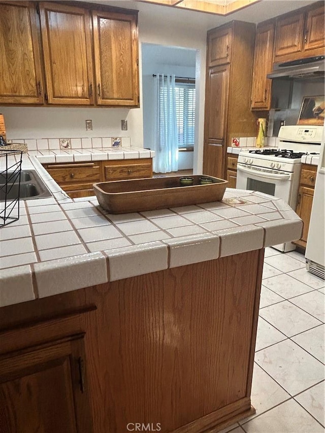 2035 N Spruce Ave, Rialto, CA 92377 - kitchen featuring tile counters, under cabinet range hood, light tile patterned flooring, white gas range oven, and a peninsula