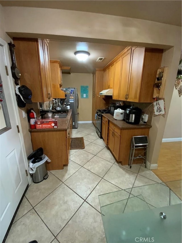 12536 Fineview St, El Monte, CA 91732 - kitchen featuring freestanding refrigerator, under cabinet range hood, gas stove, light tile patterned floors, and brown cabinets