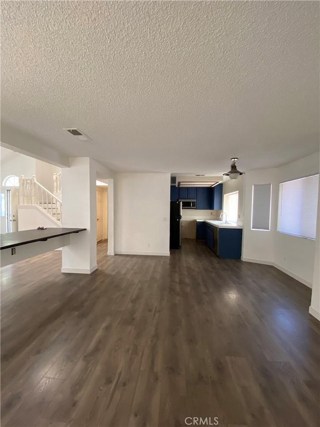 43321 Cottage Ln, Lancaster, CA 93536 - unfurnished living room featuring a textured ceiling, a sink, dark wood-style floors, stairs, and baseboards