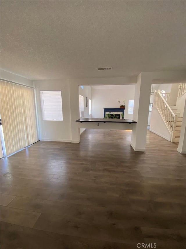 43321 Cottage Ln, Lancaster, CA 93536 - unfurnished living room featuring a textured ceiling, a fireplace with raised hearth, stairs, dark wood finished floors, and baseboards