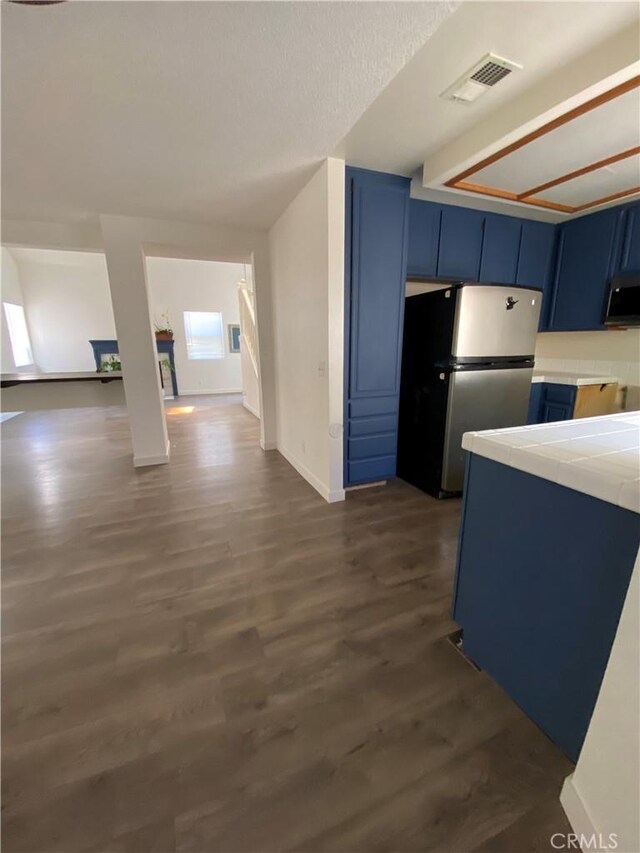 43321 Cottage Ln, Lancaster, CA 93536 - kitchen with blue cabinetry, freestanding refrigerator, tile counters, and dark wood-style floors