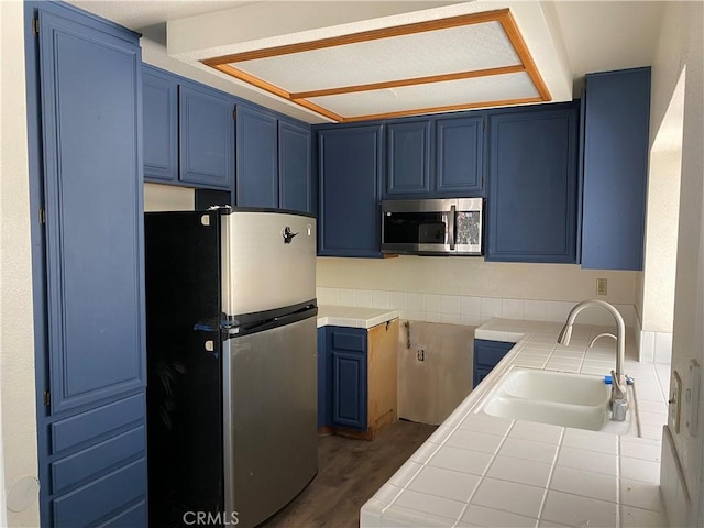 43321 Cottage Ln, Lancaster, CA 93536 - kitchen with stainless steel appliances, blue cabinetry, tile counters, and dark wood-style floors