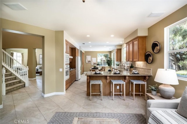 44035 Cindy Cir, Temecula, CA 92592 - kitchen featuring a peninsula, light stone counters, brown cabinetry, white appliances, and recessed lighting