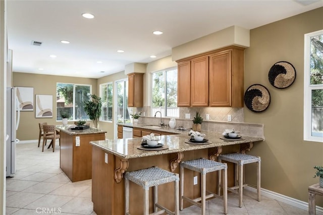 44035 Cindy Cir, Temecula, CA 92592 - kitchen featuring a kitchen island, light stone countertops, light tile patterned floors, brown cabinets, and backsplash
