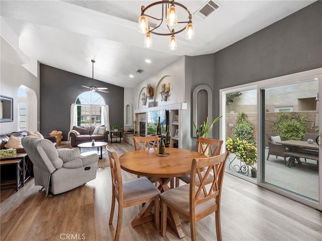 13290DR Country Club Dr, Victorville, CA 92395 - dining space featuring light wood-style floors, a chandelier, a stone fireplace, high vaulted ceiling, and arched walkways