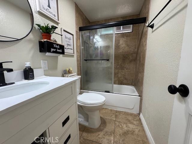 3400 Glasgow Cir, Riverside, CA 92503 - full bath with vanity, toilet, shower / bath combination with glass door, baseboards, and a textured wall