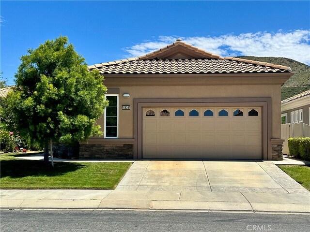 5836 Indian Canyon Dr, Banning, CA 92220 - view of front of house featuring a front yard, an attached garage, a tile roof, stucco siding, and stone siding