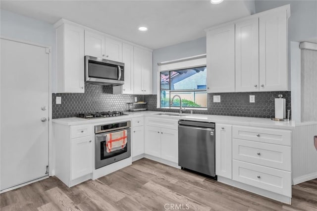26834 Pinckney Way, Menifee, CA 92586 - kitchen with stainless steel appliances, a sink, white cabinetry, light wood-type flooring, and backsplash
