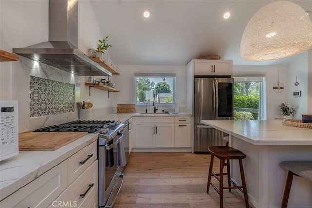 11101 Blix St, Toluca Lake, CA 91602 - kitchen featuring wall chimney exhaust hood, appliances with stainless steel finishes, a breakfast bar, light wood-type flooring, and healthy amount of natural light