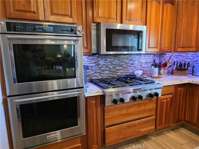 42036 Desert Sage Ave, Lancaster, CA 93536 - kitchen featuring stainless steel appliances, brown cabinets, light stone counters, and decorative backsplash