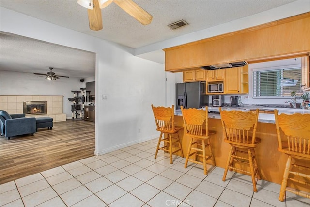 1210 3rd St, Calimesa, CA 92320 - kitchen with black refrigerator with ice dispenser, a ceiling fan, stainless steel microwave, a textured ceiling, and a kitchen breakfast bar