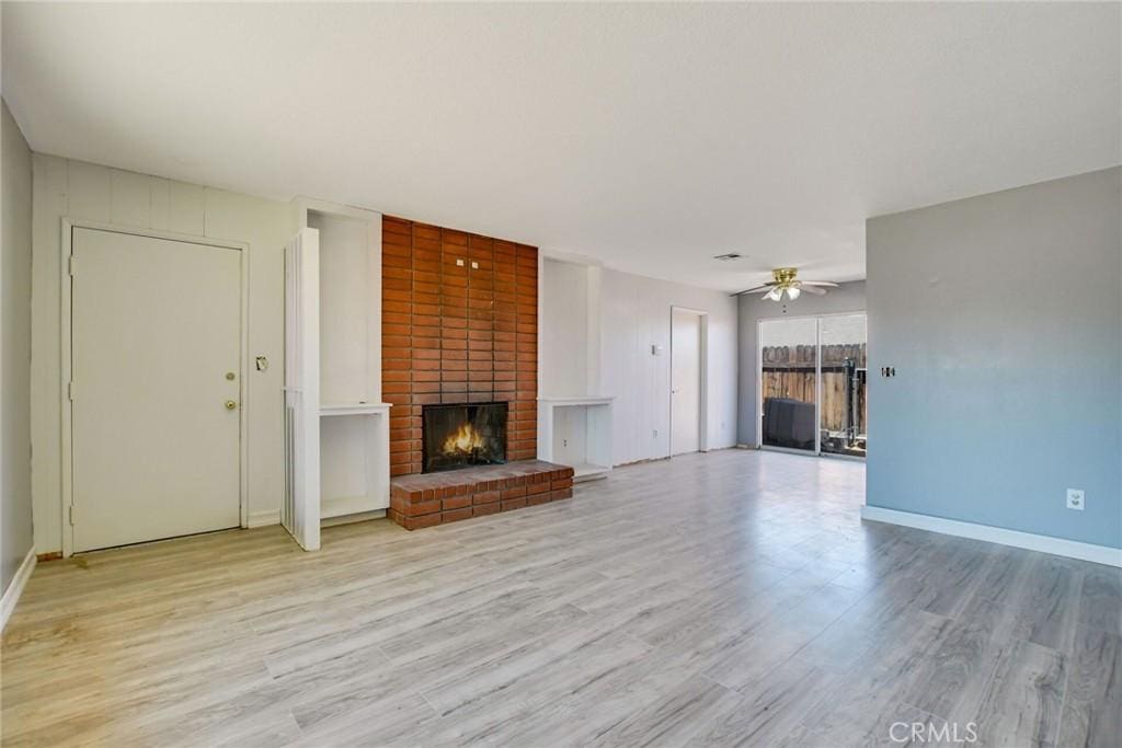 13388 Mohawk Rd, Apple Valley, CA 92308 - unfurnished living room featuring light wood-style flooring, a ceiling fan, a brick fireplace, and baseboards