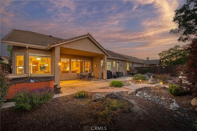 2737 Sussex Ave, Clovis, CA 93611 - back of property at dusk featuring a hot tub, a patio area, stucco siding, and a tiled roof