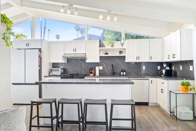 19842 Gilmore St, Woodland Hills, CA 91367 - kitchen featuring freestanding refrigerator, dishwasher, dark countertops, under cabinet range hood, and light wood-type flooring