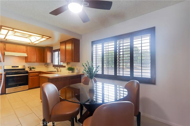 949 W Imperial Blvd Unit 14C, La Habra, CA 90631 - kitchen with stainless steel range with gas stovetop, under cabinet range hood, light countertops, a peninsula, and brown cabinets