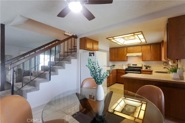 949 W Imperial Blvd Unit 14C, La Habra, CA 90631 - kitchen with stainless steel range with gas cooktop, under cabinet range hood, freestanding refrigerator, brown cabinetry, and light countertops