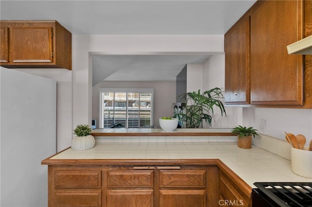 949 W Imperial Blvd Unit 14C, La Habra, CA 90631 - kitchen with freestanding refrigerator, tile countertops, brown cabinetry, and a peninsula