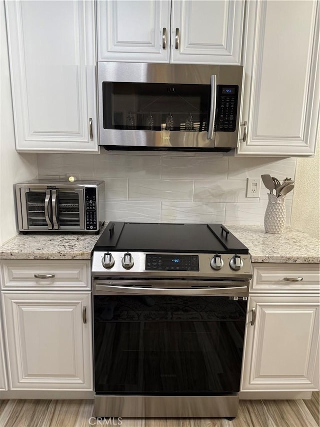41410 Juniper St Unit 2012, Murrieta, CA 92562 - kitchen with appliances with stainless steel finishes, white cabinetry, tasteful backsplash, and light stone counters