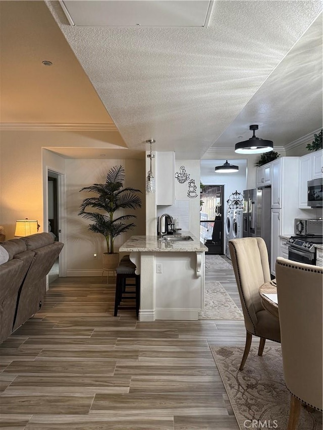 41410 Juniper St Unit 2012, Murrieta, CA 92562 - kitchen featuring white cabinets, a breakfast bar, appliances with stainless steel finishes, a peninsula, and a textured ceiling