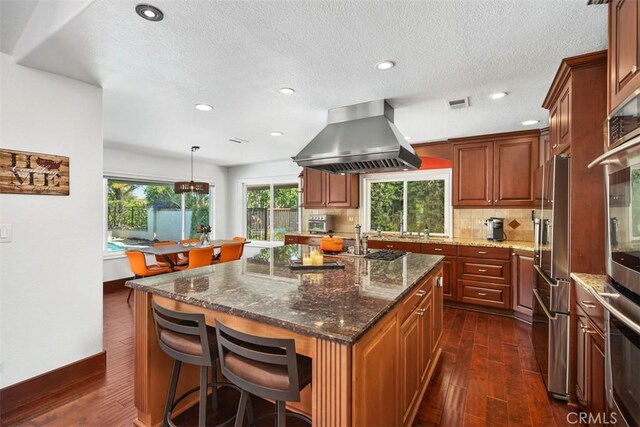 27121 Shenandoah Dr, Laguna Hills, CA 92653 - kitchen with extractor fan, dark wood-style flooring, stainless steel appliances, backsplash, and a kitchen breakfast bar