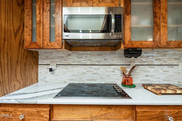 51793 Quail Ridge Rd, Oakhurst, CA 93644 - kitchen with stainless steel microwave, black electric cooktop, brown cabinetry, and tasteful backsplash