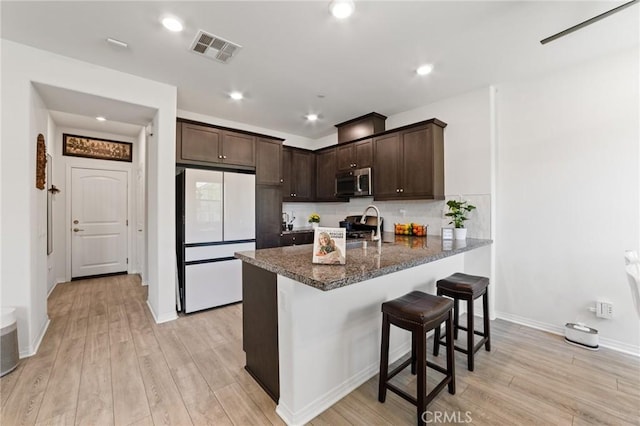 16502 Casa Grande Ave Unit 109, Fontana, CA 92336 - kitchen with freestanding refrigerator, stainless steel microwave, dark brown cabinetry, light wood-style floors, and dark stone counters