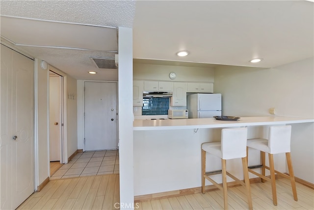 277 E Alejo Rd Unit 212, Palm Springs, CA 92262 - kitchen with white appliances, a peninsula, white cabinetry, a kitchen breakfast bar, and light countertops