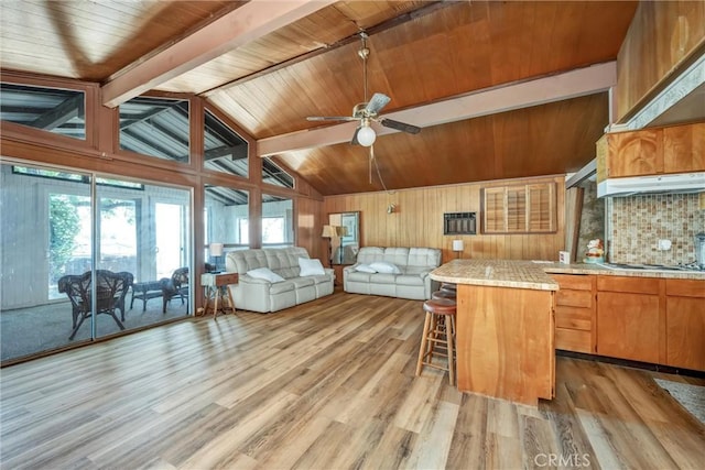 11970 N Dr, Clearlake, CA 95422 - kitchen with light wood-style floors, a breakfast bar area, a ceiling fan, under cabinet range hood, and wooden walls