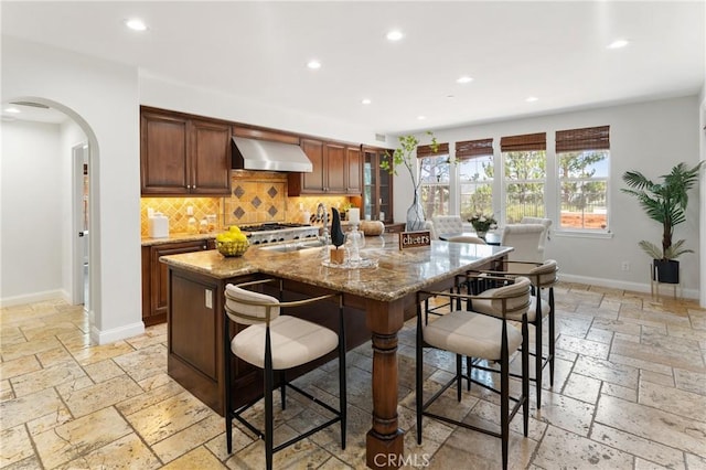15 Basilica Pl, Ladera Ranch, CA 92694 - kitchen with wall chimney range hood, stone tile floors, recessed lighting, arched walkways, and decorative backsplash