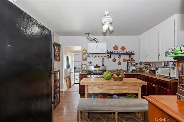 112 W Grandview Dr, Barstow, CA 92311 - kitchen featuring white microwave, stainless steel gas stove, white cabinetry, wood finished floors, and open shelves