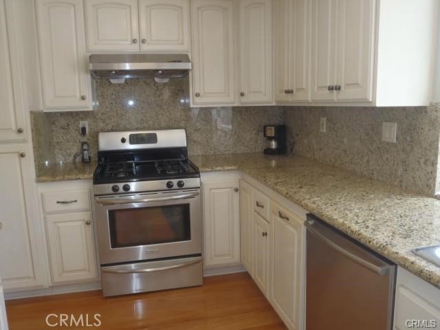 11459 Shippigan Way, Cypress, CA 90630 - kitchen featuring appliances with stainless steel finishes, under cabinet range hood, backsplash, and light stone countertops