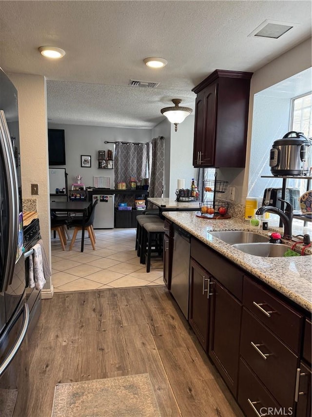 2651 Annapolis Cir, San Bernardino, CA 92408 - kitchen featuring a sink, a textured ceiling, dark brown cabinetry, stainless steel dishwasher, and wood finished floors
